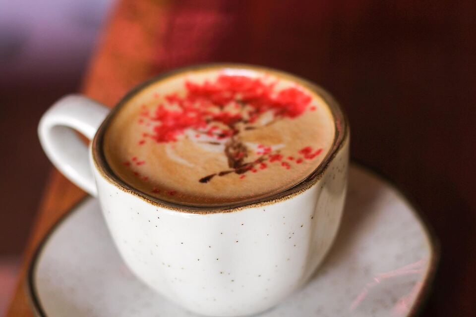 Cappuccino com desenho vermelho na espuma, numa xícara branca pontilhada