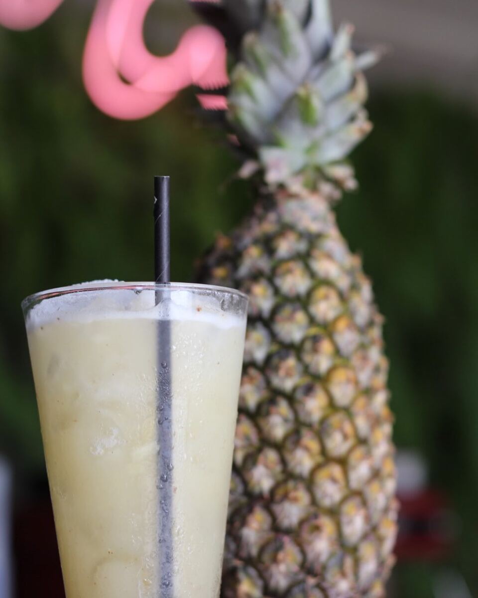 Drink cremoso de abacaxi num copo alto com canudo, ao lado de um abacaxi inteiro