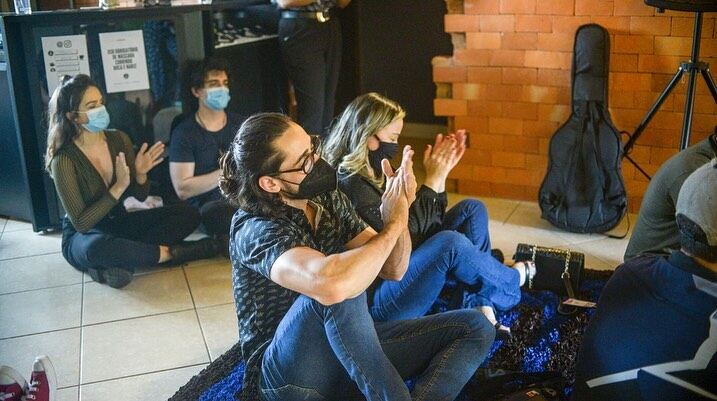 Plateia sentada no chão aplaudindo durante uma apresentação na sala de tijolos