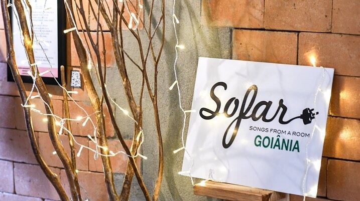 Placa do Sofar Sounds Goiânia apoiada na parede de tijolo, entre galhos secos e luzinhas